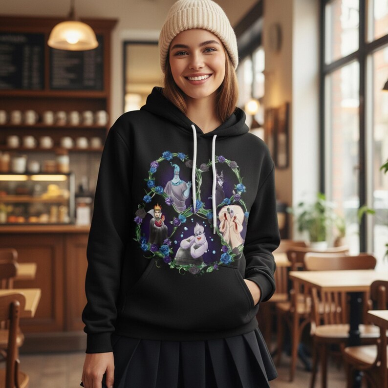 May include: Black hooded sweatshirt featuring a heart-shaped design with cartoon villains. The design includes characters in a floral wreath with blue and purple accents. The sweatshirt has a white drawstring and a front pocket.
