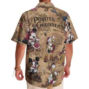 May include: A tan short-sleeved button-up shirt with a print of a treasure map featuring Mickey Mouse, Donald Duck, and other Disney characters. The shirt has the text "Disney Pirates of the Caribbean" printed on the front.