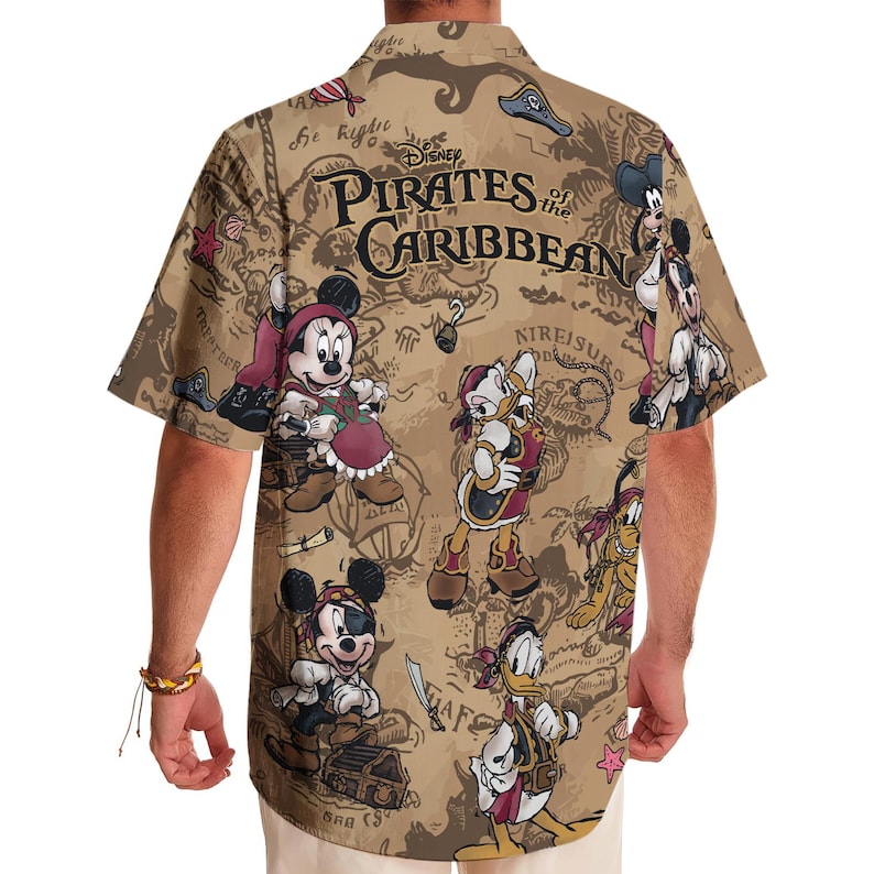 May include: A tan short-sleeved button-up shirt with a print of a treasure map featuring Mickey Mouse, Donald Duck, and other Disney characters. The shirt has the text "Disney Pirates of the Caribbean" printed on the front.