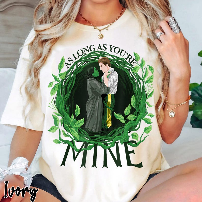 May include: Ivory t-shirt with a graphic of two figures embraced within a green leafy wreath. The text "AS LONG AS YOU'RE" arches above the figures, with "MINE" below. The design is centered on the shirt.