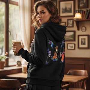 May include: Black hooded sweatshirt with a colorful graphic on the back. The graphic features a lion and other characters surrounded by blue and purple flowers. The sweatshirt has a drawstring hood and a white drawstring.