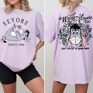May include: A lavender t-shirt with a graphic of Eeyore from Winnie the Pooh. The front of the shirt says "Eeyore Since 1966". The back of the shirt says "Weeds are flowers too. Once you get to know them."