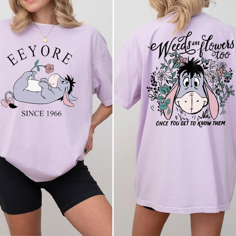 May include: A lavender t-shirt with a graphic of Eeyore from Winnie the Pooh. The front of the shirt says "Eeyore Since 1966". The back of the shirt says "Weeds are flowers too. Once you get to know them."