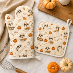 May include: A cream-colored oven mitt and a square pot holder featuring a repeating pattern of puppies wearing chef hats, pumpkins, whisks, and cookies. The text Luna is printed in a cursive script throughout the fabric design.