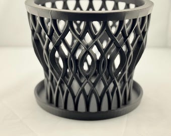 May include: Black plastic planter with a geometric design. The planter has a wide base and a narrow top, creating a funnel shape.