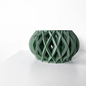 May include: A green decorative bowl with a geometric diamond pattern. The bowl has an oval shape and is made of a solid material. The design features open spaces, creating a unique visual effect. The bowl is placed on a white surface.