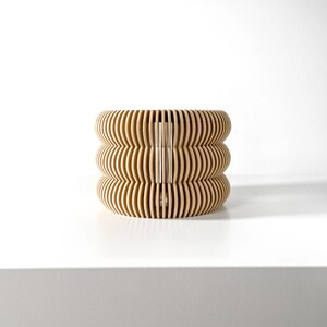 May include: A light brown wooden lampshade with a geometric pattern. The lampshade is made of thin, curved slats that create a unique and modern design.