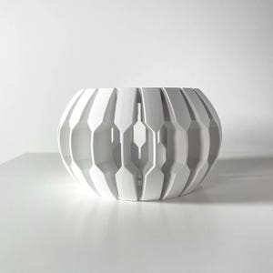 May include: A white ceramic bowl with a geometric design. The bowl has a rounded shape and is made of a smooth, white material.