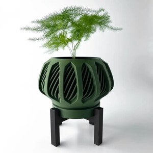 May include: A dark green planter with a geometric design and a black stand. The planter is filled with a green plant.