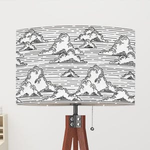 May include: A floor lamp with a brown wooden tripod base and a rectangular lampshade. The lampshade features a black and white cloud pattern. The lamp has a pull chain and is suitable for home decor.