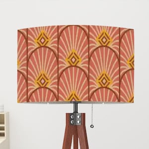 May include: A floor lamp with a brown wooden tripod base and a rectangular lampshade. The lampshade features a repeating geometric pattern in shades of coral, yellow, and white. The lamp has a pull chain and is designed for indoor use.