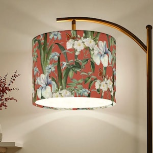May include: A floor lamp with a floral lampshade. The lampshade features a red background with white, blue, and green floral patterns. The lamp has a curved, gold-colored arm and a dark brown base.
