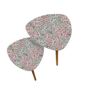 May include: Two small, triangular side tables with a floral pattern. The tables have a light pink, blue, and green hydrangea design on the tabletop. The legs are made of a light brown wood.