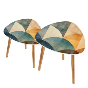May include: Two triangular side tables with a watercolor design in shades of blue, tan, and orange. The tables have white edges and light brown wooden legs. The tables are a decorative accent for a living room or bedroom.