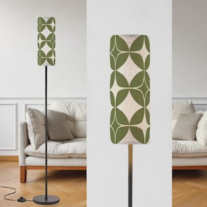 May include: A tall, modern floor lamp with a cylindrical lampshade. The shade features a repeating pattern of green leaf-like shapes on a cream background. The lamp has a black metal pole and a round base, with a foot switch.
