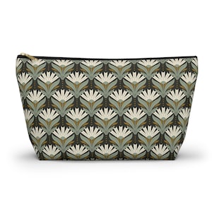 May include: A zipped pouch featuring a repeating floral design in cream, sage green, and gold on a dark background. It has a black zip and trim.