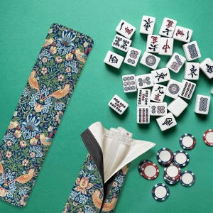 以下が含まれることがあります： 緑色の表面に置かれた麻雀セット。セットには、黒と赤のマークが付いた白いタイル、模様入りのケース、ポーカーチップが含まれています。ケースには、鳥のいる青い花柄のデザインがあります。