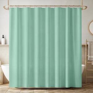 Puede incluir: Una cortina de ducha verde menta lisa cuelga de una barra dorada. La cortina está hecha de una tela suave y tiene pliegues verticales. El baño incluye una bañera blanca, un suelo de madera y una estantería con una botella blanca.