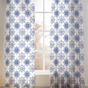 May include: White nautical-themed curtains with a repeating pattern of blue ship wheels. The curtains are hanging in front of a window, creating a decorative and functional window treatment. The design adds a coastal touch to any room.