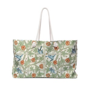 May include: A large tote bag with a white rope handle. The bag features a repeating pattern of blue birds, orange flowers, and green leaves on a cream background. The design is reminiscent of vintage botanical illustrations.