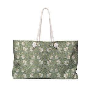 Peut inclure: Un grand sac fourre-tout arborant un motif botanique répétitif de fleurs blanches et de feuillage vert sur un fond vert sauge. Le sac possède deux anses en corde blanche fixées par des œillets métalliques argentés sur le bord supérieur rectangulaire.