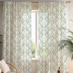 May include: White and green patterned curtains. The curtains feature a repeating design of stylized green leaves and swirls against a white background. The curtains are hanging in front of a window, with a glimpse of the outside visible.