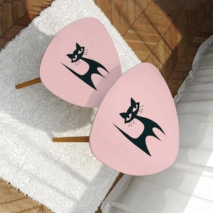 May include: Two pink, triangular shaped side tables with black cat silhouettes on the top. The tables have wooden legs.