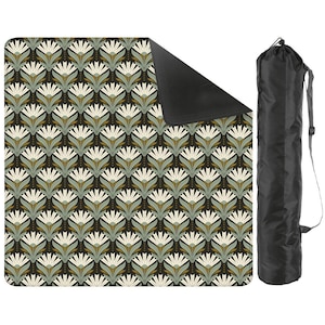 Könnte beinhalten: Eine Picknickdecke mit Muster und eine schwarze Tragetasche. Die Decke hat ein sich wiederholendes Blumendesign in Weiß, Grün und Gold auf einem dunkelbraunen Hintergrund. Die Tasche ist schwarz mit einem Schultergurt.