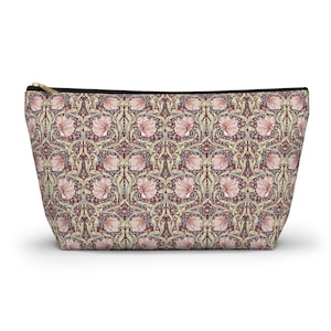 Puede incluir: Un neceser rectangular con un estampado floral en tonos rosa, burdeos y verde. El neceser tiene una cremallera negra y un tirador dorado. El neceser está diseñado para mantenerse de pie.