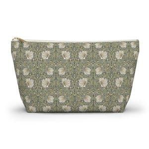 May include: A rectangular cosmetic bag with a floral pattern. The bag features a repeating design of white flowers and green leaves on a sage green background. A gold-colored zipper runs along the top.