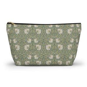 Peut inclure: Une pochette zippée présentant un motif botanique répétitif de fleurs crème et de feuillage vert sur un fond vert sauge. L'accessoire possède une fermeture éclair noire sur le bord supérieur et une forme trapézoïdale avec une base large.