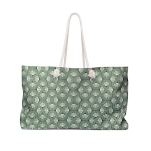 May include: Large tote bag featuring a repeating fan-shaped pattern in green and cream. It has white rope handles and white decorative knots. The bag is designed for carrying items. The bag's dimensions are approximately 60 cm in length.