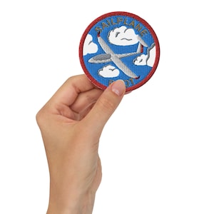 Può includere: Una toppa ricamata blu e bianca con un bordo rosso. La toppa presenta un aliante che vola tra le nuvole e il testo "Sailplane Pilot".