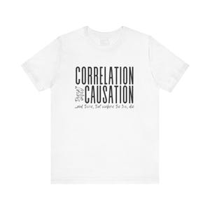 May include: White t-shirt with black text that reads "Correlation Doesn't Imply Causation... and those that confuse the two, die."
