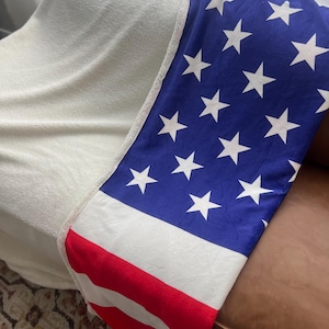 May include: A white and blue blanket with red stripes and white stars, folded over a brown leather couch.