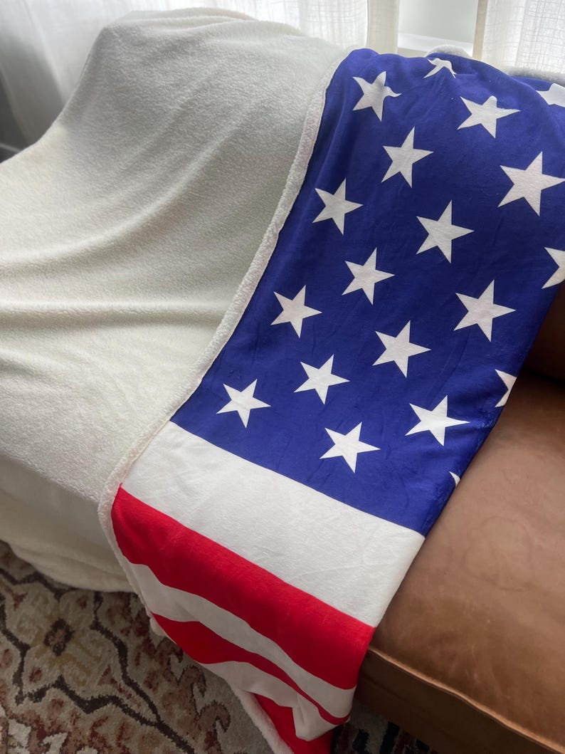 May include: A white and blue blanket with red stripes and white stars, folded over a brown leather couch.
