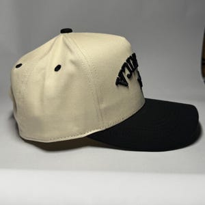 K&ouml;nnte beinhalten: Beige-schwarze Baseballkappe mit dem Wort "RICA" in Schwarz auf der Vorderseite gestickt. Die Kappe hat eine strukturierte Krone und einen gebogenen Schirm. Hergestellt aus strapazierf&auml;higem Stoff.