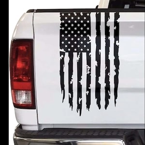 Puede incluir: Una camioneta blanca con una calcomanía de bandera estadounidense desgastada en blanco y negro en la puerta trasera.