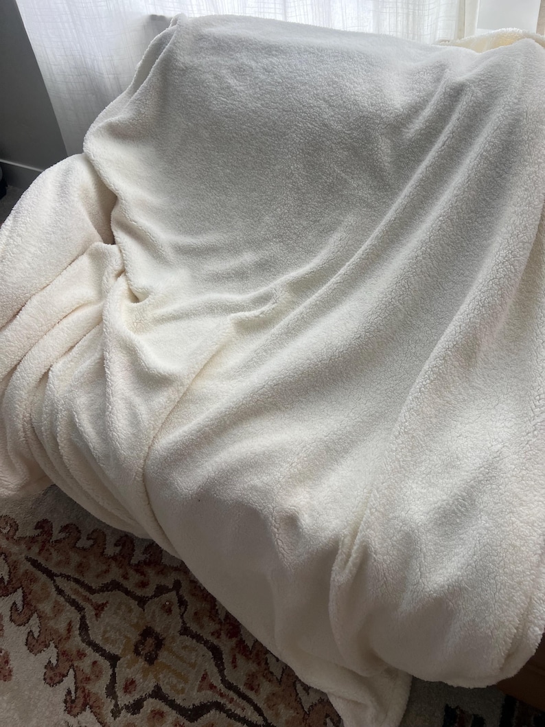 May include: A white fluffy blanket draped over a chair. The blanket is soft and plush, perfect for cuddling up on a cold day.