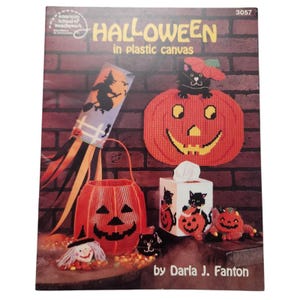 Pode incluir: Uma capa de livro intitulada "Halloween in plastic canvas" com vários artesanatos de Halloween em tela plástica. Os artesanatos incluem uma abóbora, uma bruxa em uma vassoura, uma cesta de abóbora e uma caixa de lenços com desenhos de gatos pretos. A autora é Darla J. Fanton.