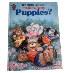 Puede incluir: Un libro infantil titulado "What's So Funny, Puppies?" presenta una portada azul con ilustraciones de cachorros de dibujos animados juguetones. Los cachorros son de varios colores y atuendos, sobre un fondo floral. El libro es de la serie "Itsy-Bitsies Storybooks".