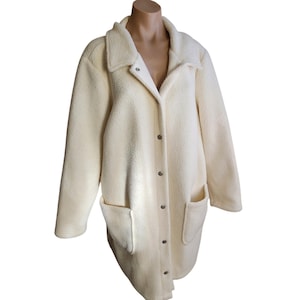 May include: A cream-colored fleece jacket featuring a collared neckline, long sleeves, and a front button-down closure with silver-toned metal snaps. The jacket includes two large patch pockets on the front and a soft, textured fabric finish.