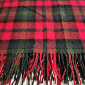 May include: A tartan scarf in red, black, and green. The scarf has a classic plaid design with large red squares and black and green intersecting lines. The bottom edge is finished with a fringe, adding a traditional touch to the accessory.
