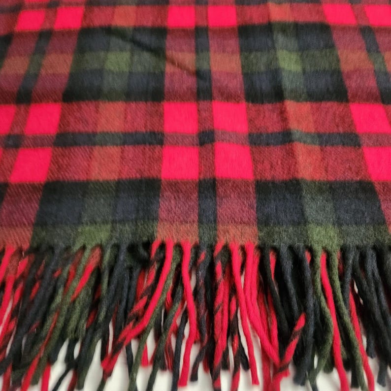 May include: A tartan scarf in red, black, and green. The scarf has a classic plaid design with large red squares and black and green intersecting lines. The bottom edge is finished with a fringe, adding a traditional touch to the accessory.