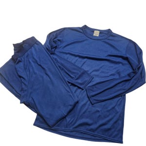 Puede incluir: Un conjunto deportivo de dos piezas en un tono azul oscuro. El conjunto incluye una camiseta de manga larga con cuello redondo y pantalones a juego. La tela parece ser un material ligero y transpirable, adecuado para ropa deportiva o para usar en capas. El conjunto está diseñado para la comodidad y la facilidad de movimiento.