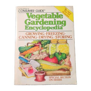 May include: A softcover book titled Vegetable Gardening Encyclopedia by the Editors of Consumer Guide. The cover features a colorful illustration of garden vegetables, canning jars, a trowel, and seed packets with the text Recipes For All Seasons.