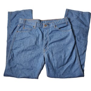 May include: A pair of medium-wash blue denim jeans featuring a classic five-pocket design, a button and zipper fly closure, belt loops along the waistband, and copper-toned metal rivets at the corners of the front pockets.