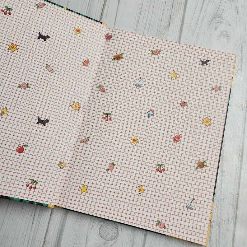 May include: An open notebook with a white grid pattern and red lines. The notebook is decorated with various small illustrations, including stars, hearts, cherries, sailboats, houses, and a sunflower.