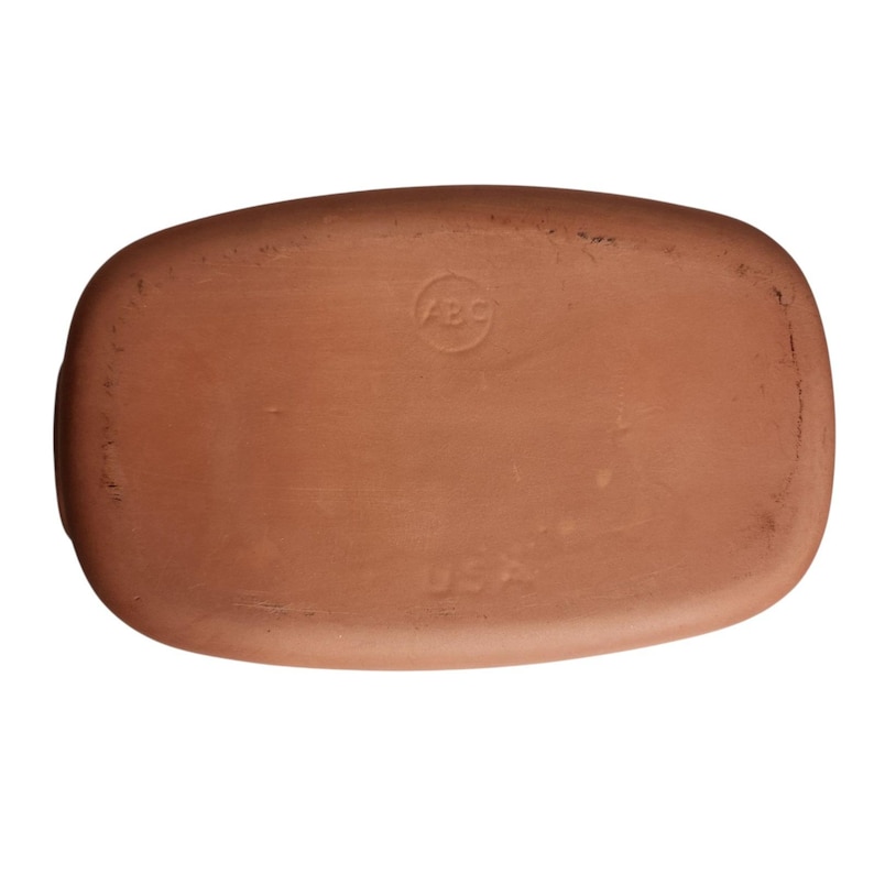 May include: A rectangular, terracotta-colored ceramic tray. The underside features a circular stamp with the letters "ABC" and the word "USA" stamped below. The tray has rounded corners and a slightly textured surface.