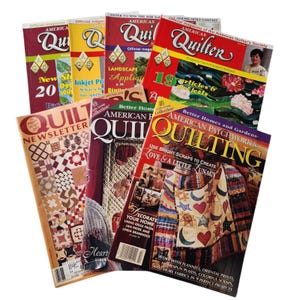 以下が含まれることがあります： 「American Quilter」や「Quilt Newsletter」などのタイトルが付いた、カラフルなキルト雑誌のコレクション。雑誌には、キルト、パッチワークのデザイン、キルティング技術に関する記事の写真が掲載されています。表紙には様々な色とデザインが表示されています。